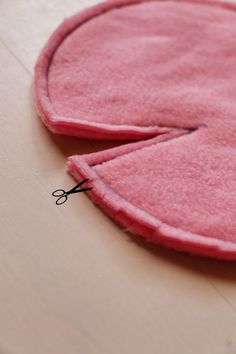 a pair of scissors cutting through the side of a pink piece of felt with two holes in it