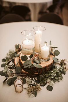 candles and greenery sit on top of a wooden slice at the center of a table