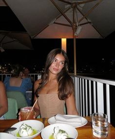 a woman sitting at a table with plates of food and drinks in front of her