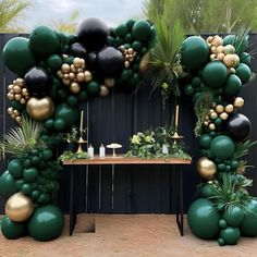 a table topped with lots of green balloons and greenery next to a black fence