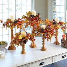 a table topped with candles and fall leaves on top of white counter tops next to windows