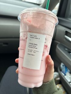 a person holding up a pink drink in their hand with information on the cup sleeve