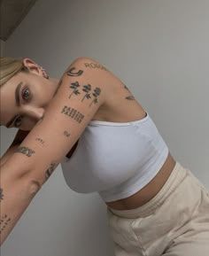 a woman with tattoos on her arm leaning against a wall