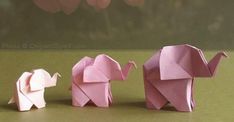 three pink origami elephants standing next to each other on a green surface with flowers in the background