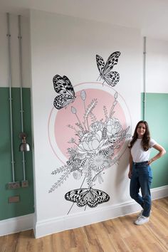 a woman standing in front of a wall with flowers and butterflies painted on the wall