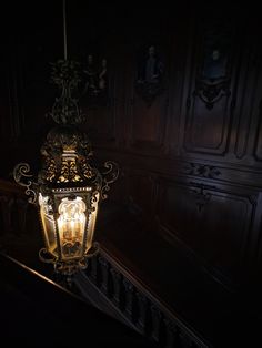 an old fashioned light hanging from the side of a stair case in a dark room