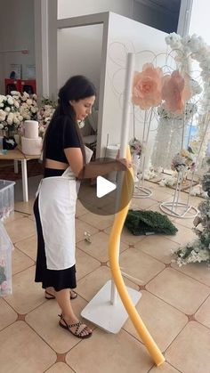 a woman standing in front of a vase with flowers on it and holding a yellow hose