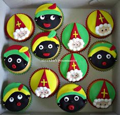 cupcakes decorated with black, yellow and red decorations in a white cardboard box