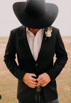 a man in a black suit and cowboy hat with his hands on his hips looking at the camera