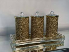 three gold glitter canisters sitting on top of a glass shelf