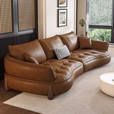 a brown leather couch sitting on top of a white rug in a living room next to a window