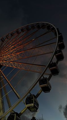 the ferris wheel is lit up at night with its lights turned on and dark clouds in the background