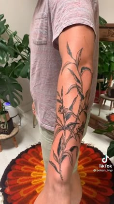 a man with a tattoo on his arm and leg is standing in front of a potted plant