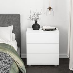 a white nightstand with a black vase on top of it next to a gray bed