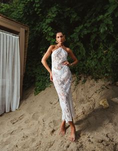 a woman standing in the sand wearing a white dress