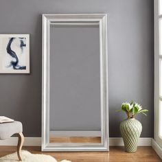 a large mirror sitting on top of a wooden floor next to a white vase filled with flowers