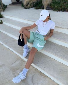 a woman sitting on the steps with her tennis racket in her hand and wearing a white hat