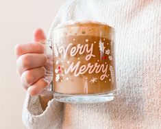 a person holding a glass mug with merry written on it