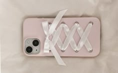 an iphone case with white ribbons attached to the back of it, on a light pink background