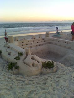 people are standing on the beach next to an elaborate sand castle