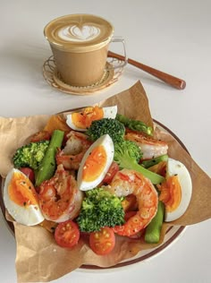 a plate with shrimp, broccoli and eggs on it next to a cup of coffee