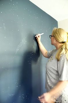 a woman is writing on the wall with a white marker and some blue walls are in the background