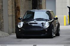 a small black car parked on the side of a road next to a brick building