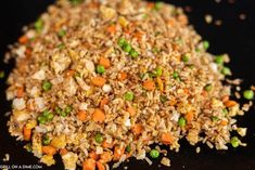 a pile of brown rice with peas and carrots on the top is sitting on a black surface