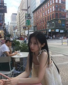 a young woman sitting at a table in the middle of a city with tall buildings