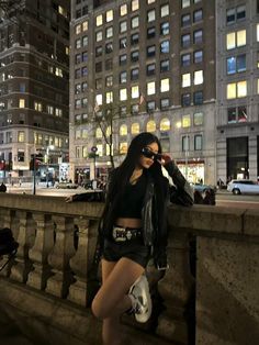 a woman in short shorts and leather jacket leaning on a wall near a city street