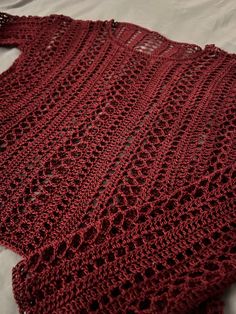 a red crocheted shawl laying on top of a bed