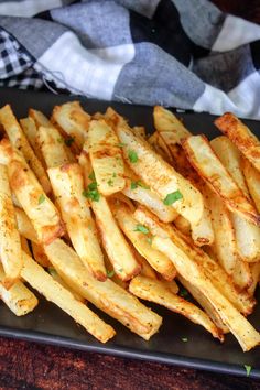 french fries on a black plate with parsley sprinkled around the edges, ready to be eaten