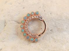 a rose gold ring with opal and diamond accents on a stone surface in front of a rock