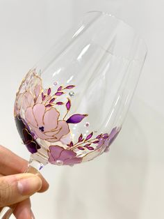 a hand holding a wine glass with flowers painted on the side and purple trimmings