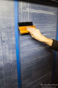 a man is painting the wall with blue paint and a yellow brush in his hand