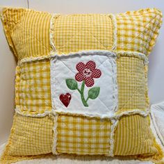 a yellow and white patchwork pillow with flowers on the front, sitting on a bed