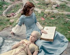 two women are laying on the ground reading books and one is holding an open book