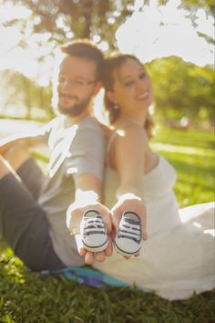 a man and woman sitting on the grass holding shoes