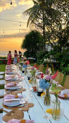 a long table is set up with plates and flowers in vases for an outdoor dinner