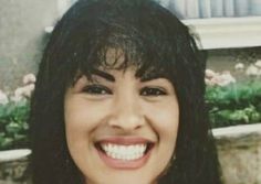 a close up of a person smiling with flowers in the backgrouund behind her