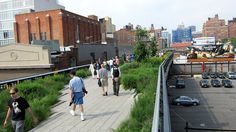 several people walking on a boardwalk near tall buildings and green roofing areas in the city