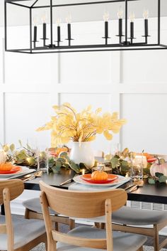 a dining room table set with plates and place settings, candles and flowers in a vase