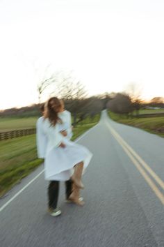 a woman walking down the middle of a road with her leg in the air and another person standing behind her