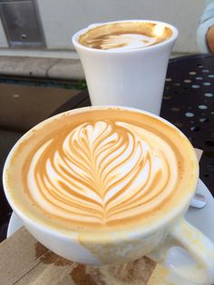 two cups of cappuccino sitting next to each other on top of a table