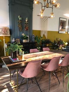 a dining room table with pink chairs in front of it and potted plants on the other side