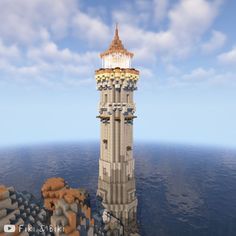 a very tall tower sitting in the middle of some water with rocks and sand around it