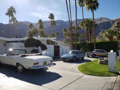 an old car parked in front of a house with palm trees and mountains in the background