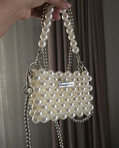 a hand holding a white purse with pearls on it