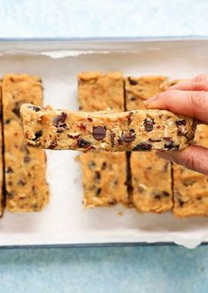 a person holding up a cookie bar with chocolate chip toppings on it, in front of a blue background