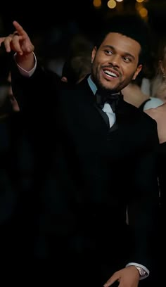 a man in a tuxedo pointing at something while standing next to a woman